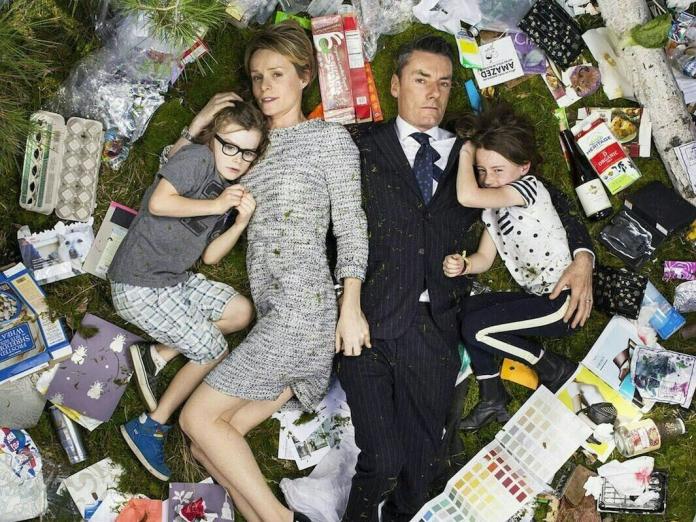 Two parent, woman and man, lying on a field of grass with one kid on each side. The grass is full of waste